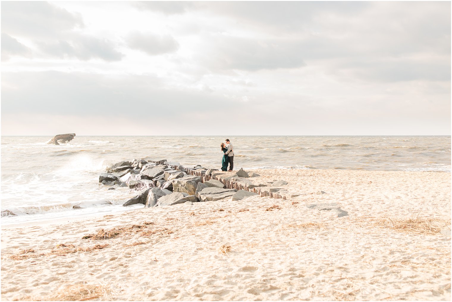 Engaged couple holding each other on a jetty at iconic Cape May beach location 