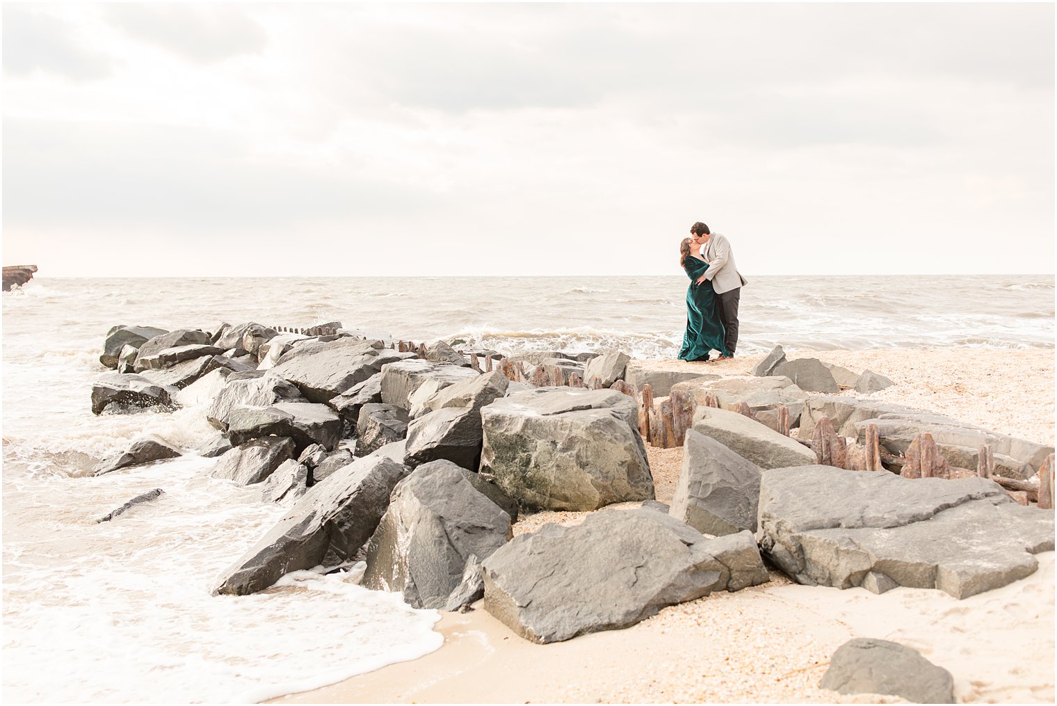 Engaged woman wearing green velvet dress from Baltic Born kissing fiance on a jetty