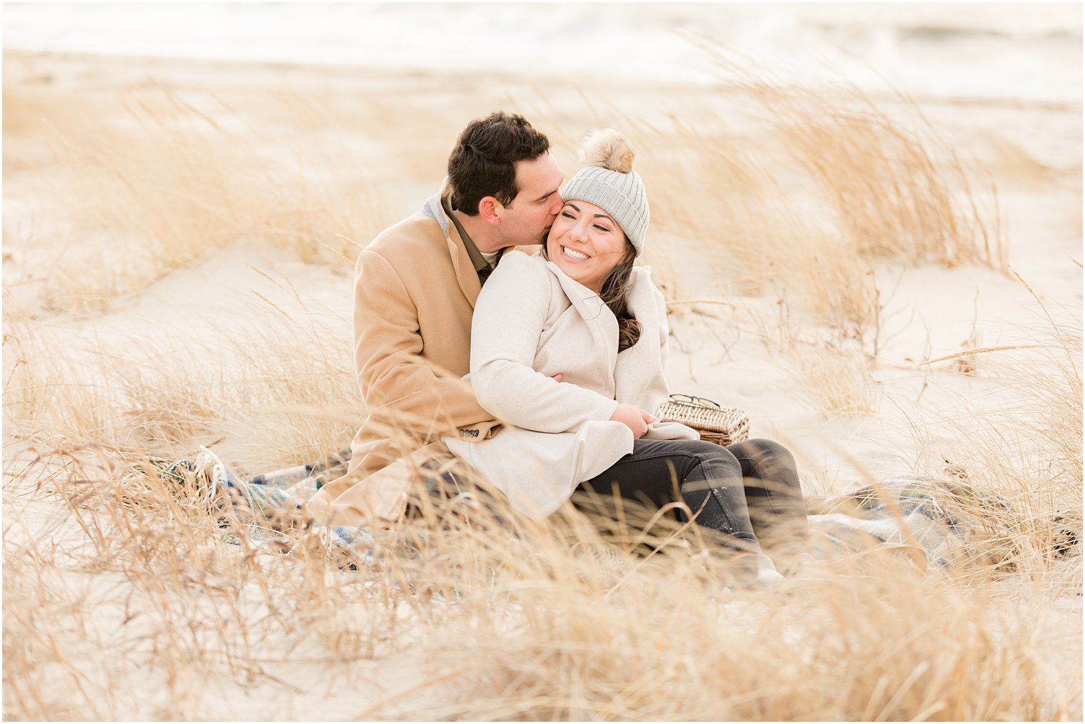 Engaged couple sitting on a plaid blanket on the beach during winter