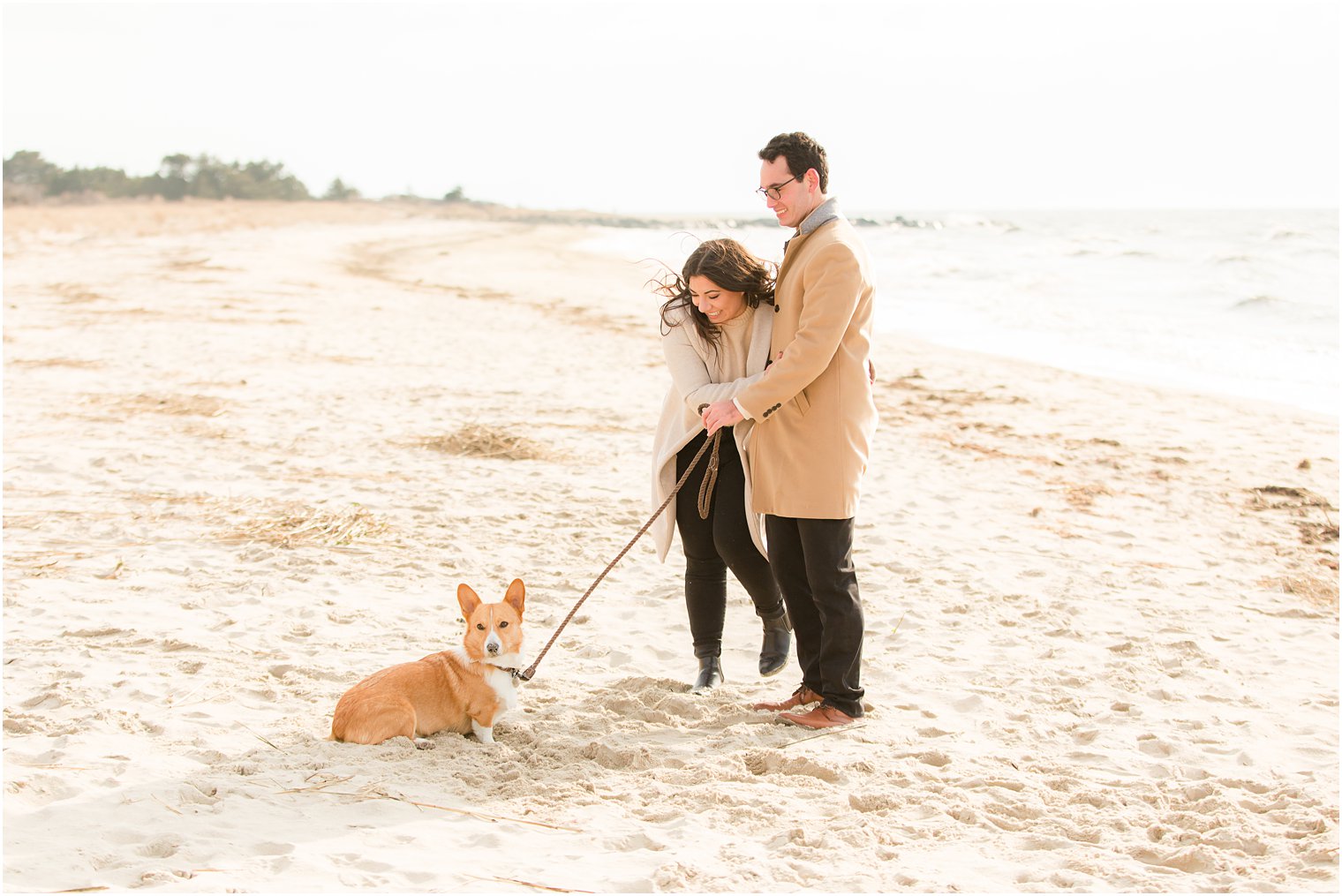 Engaged couple taking pictures with Corgi on the beach in the winter