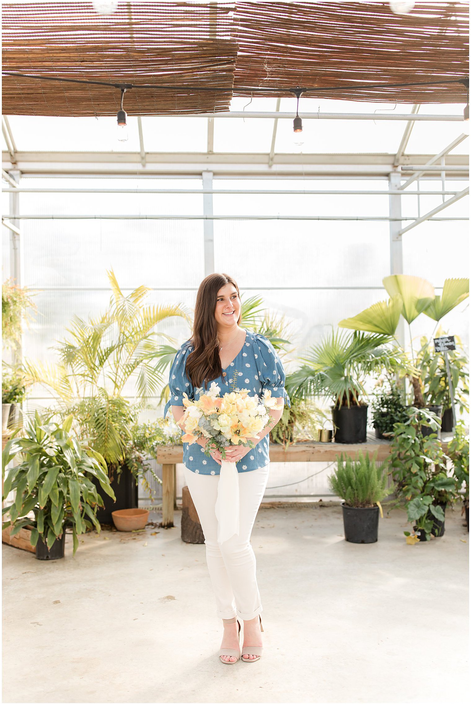 bride in blue polka dot top holds bouquet of yellow flowers at Herbary at Bear Creek