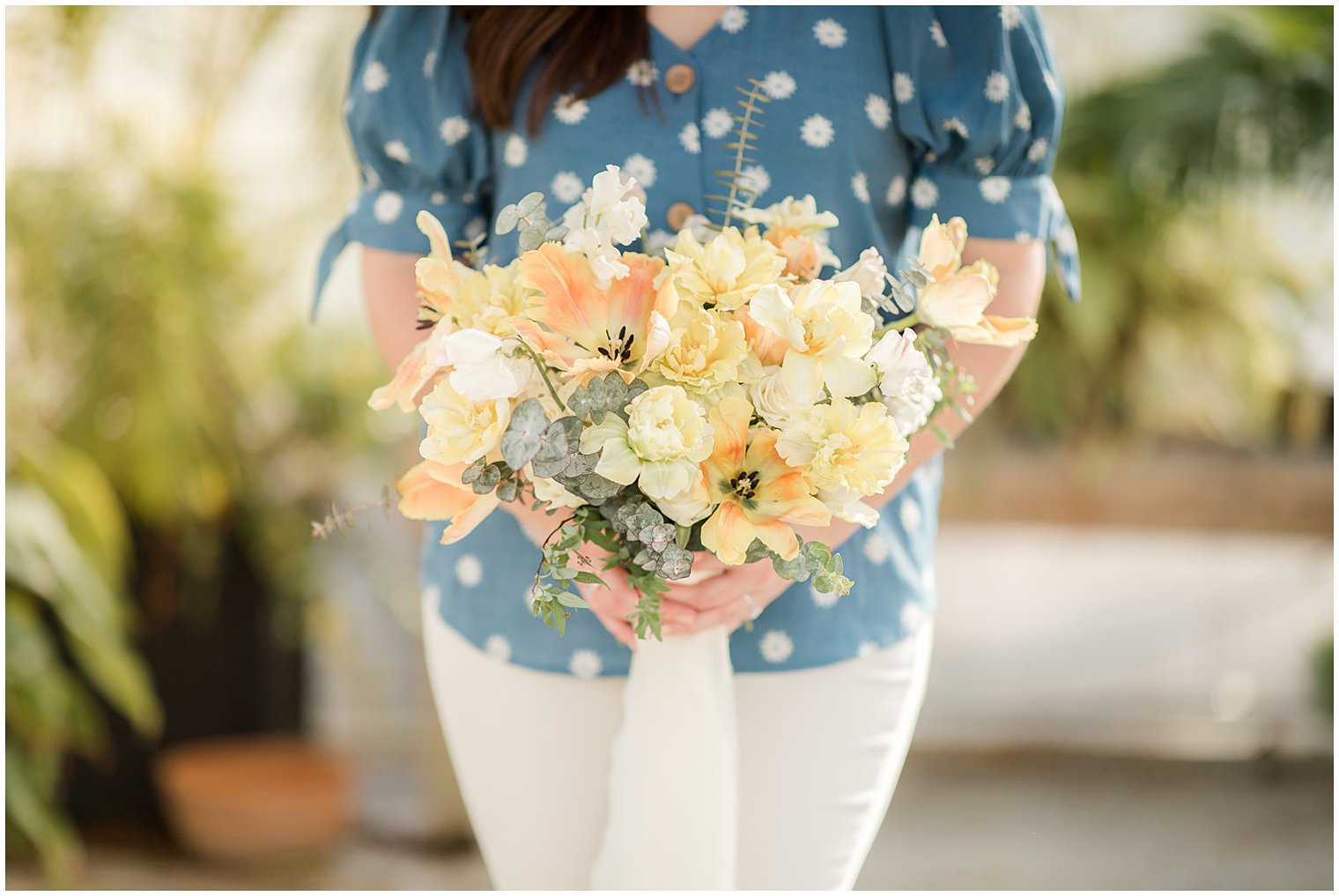 bride holds bouquet of yellow flowers for spring engagement photos in greenhouse