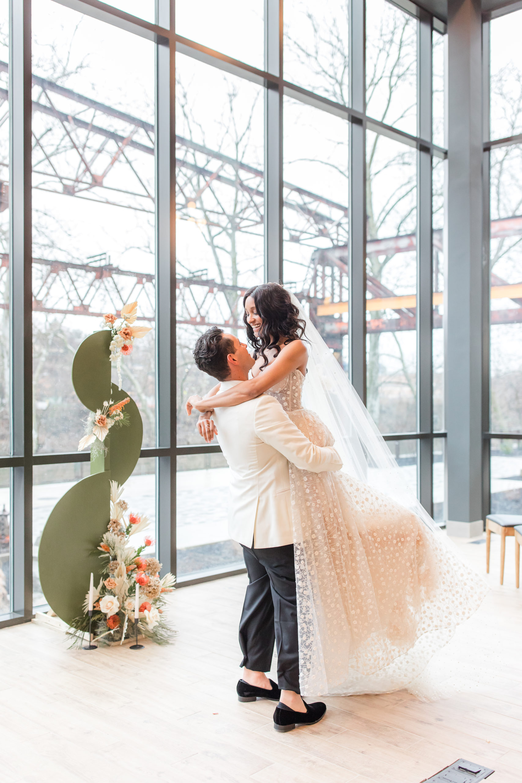 groom lifts bride with veil in front of iron windows in Philadelphia PA