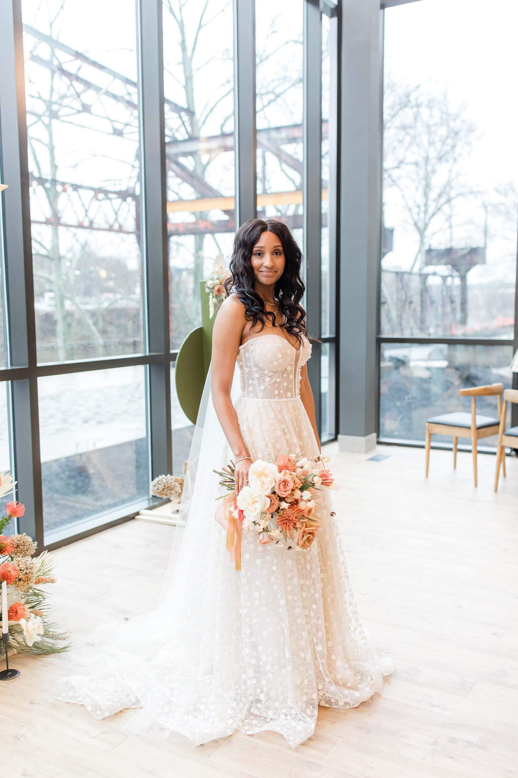 bride in wedding dress with polka dot lace overlay holds bouquet of flowers in Ironworks at Pencoyd Landing