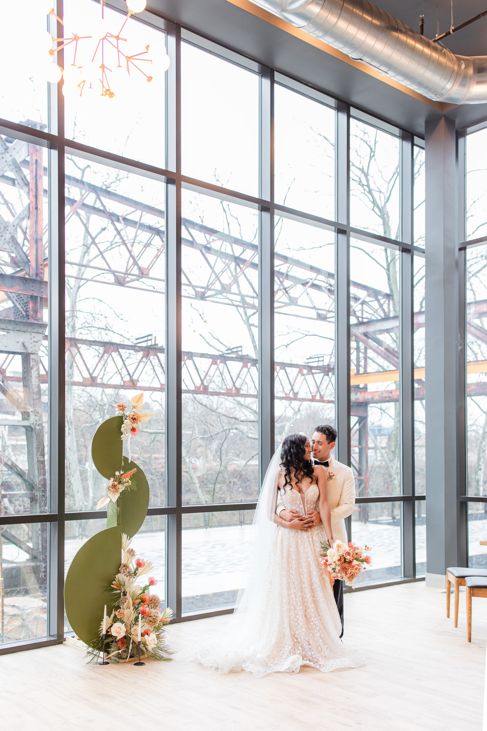 bride and groom pose by wall of windows at Ironworks at Pencoyd Landing