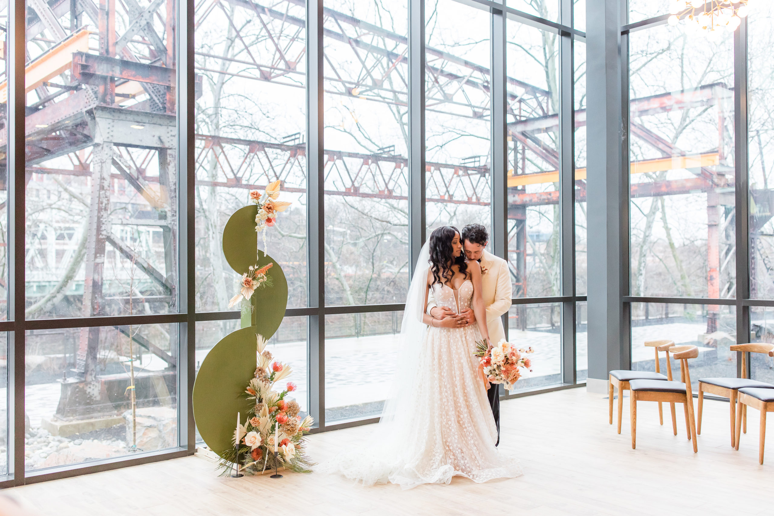 groom hugs bride kissing her shoulder during Philly PA wedding day editorial at Ironworks at Pencoyd Landing