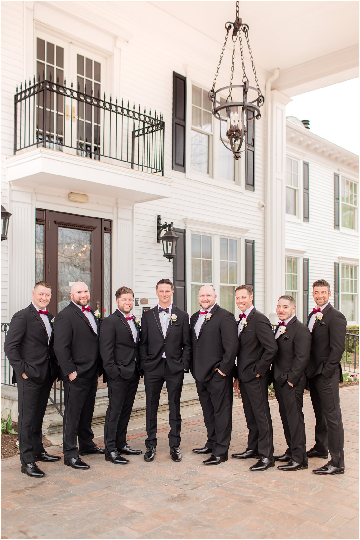 groom poses with groomsmen outside white building in New Jersey 