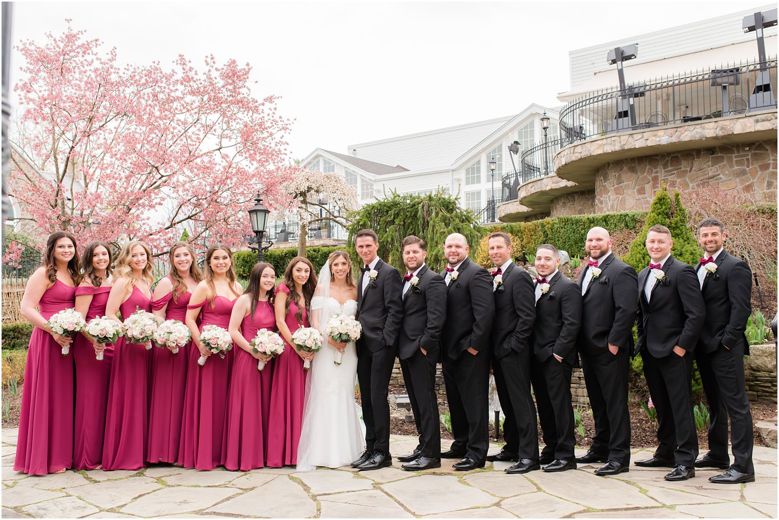 bride and groom pose with bridesmaids in cranberry and groomsmen in black suits 