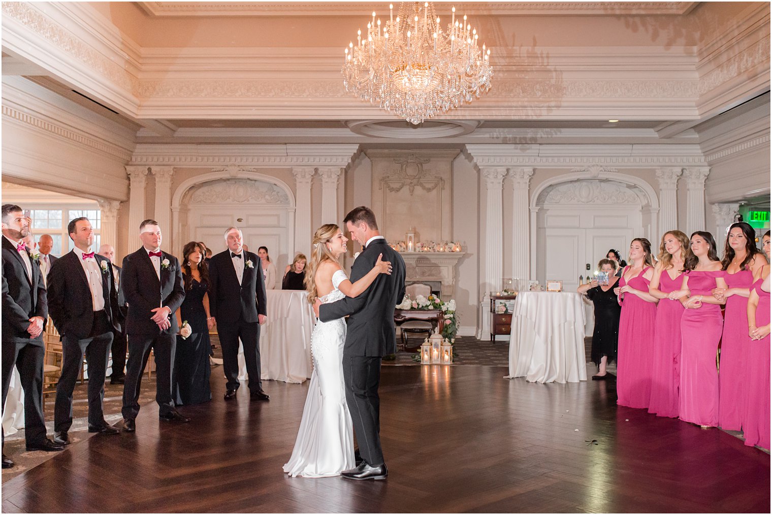 bride and groom have first dance on ballroom floor with bridal party surrounding them 