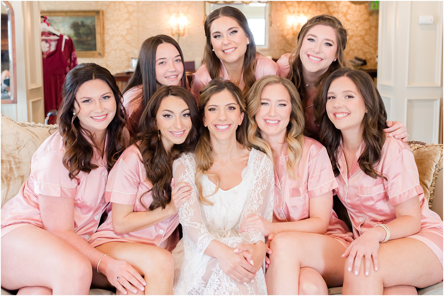 bridesmaids in matching pink robes sit on couch with bride 