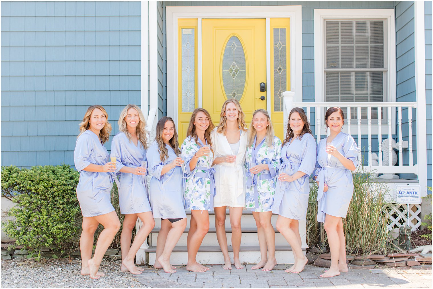 bride and bridesmaids hold champagne glasses outside yellow door 