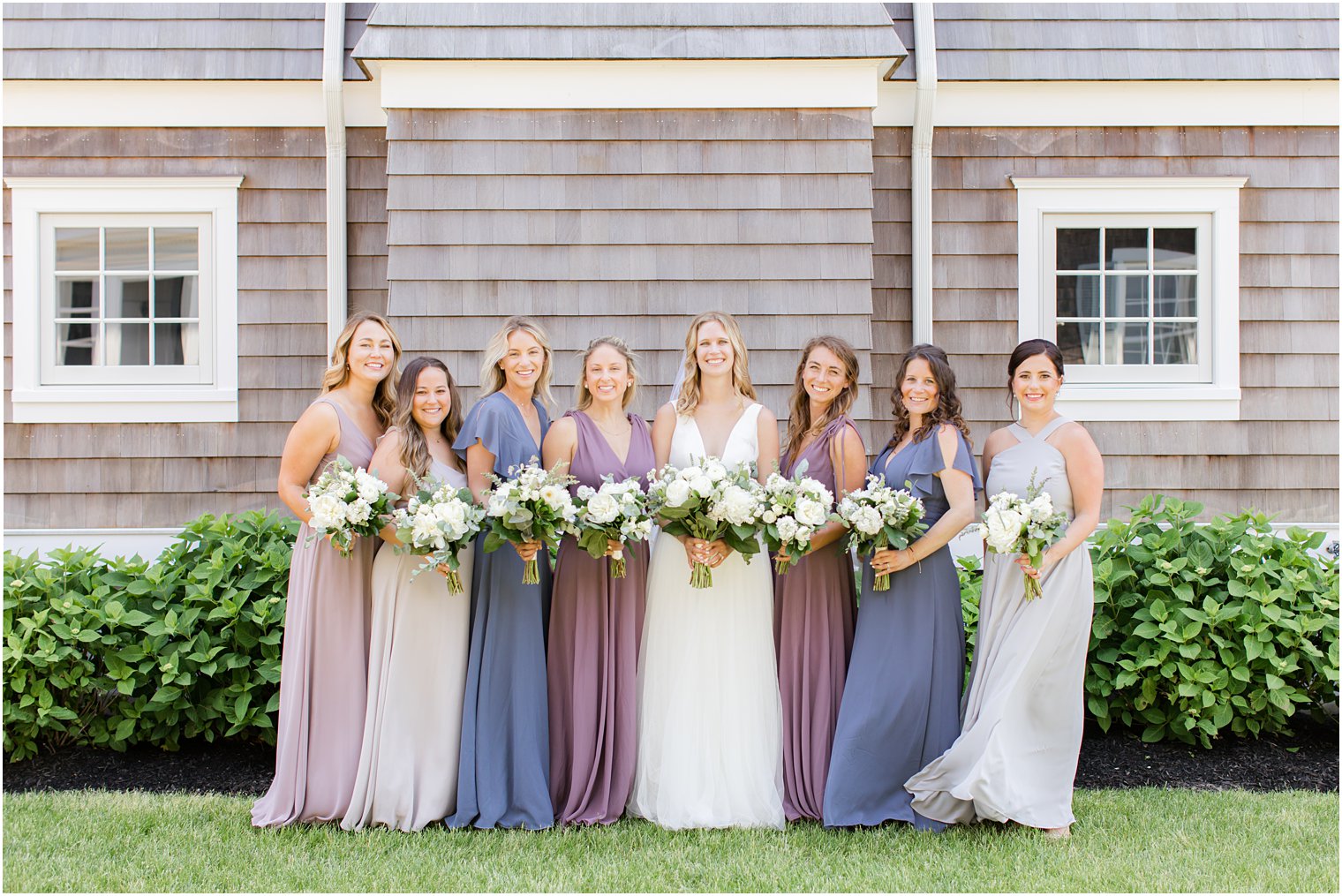 bride and bridesmaids in pink, purple and blue gowns pose outside wooden building in New Jersey 