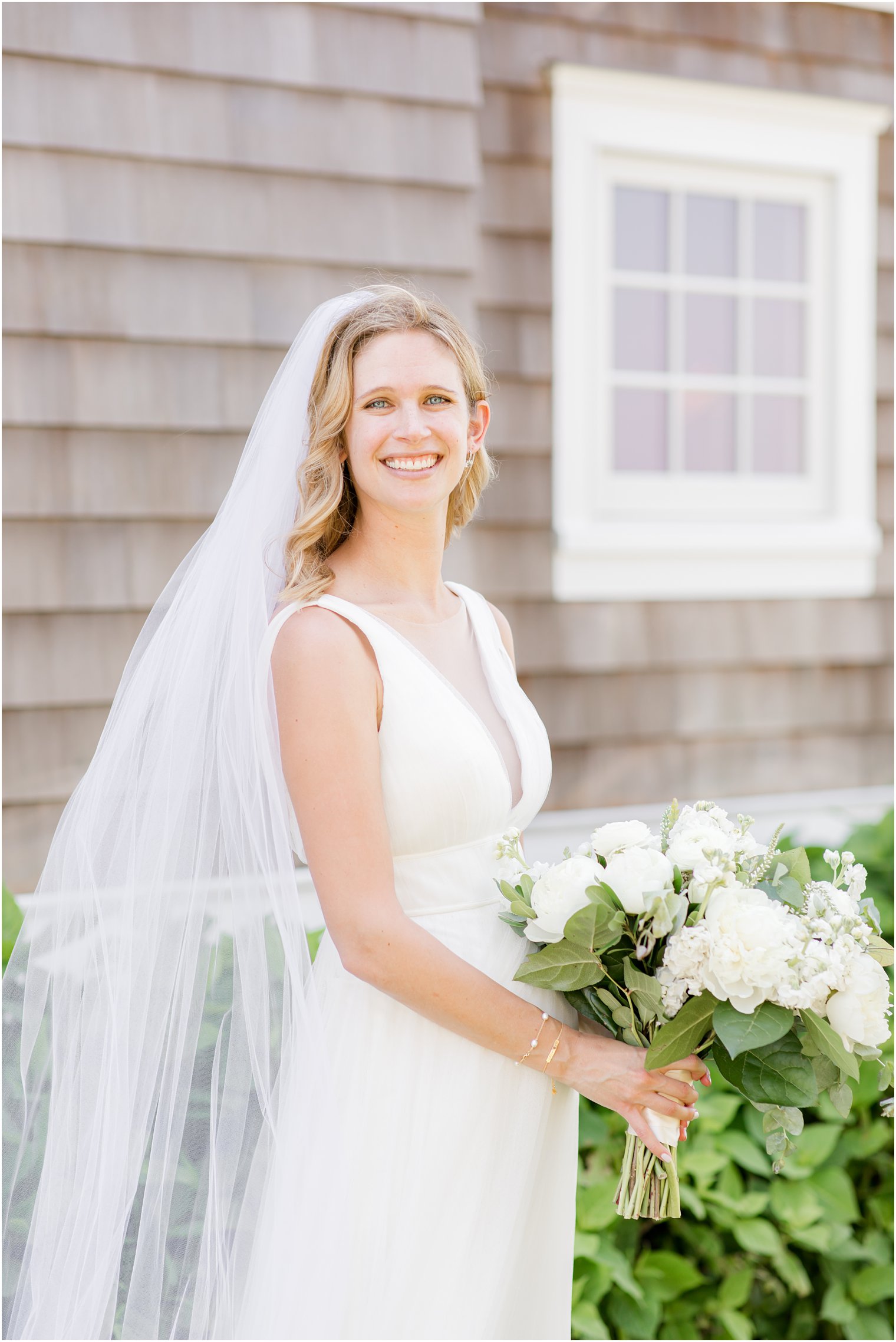 bride poses by Bay Head NJ building holding bouquet of all-white flowers 