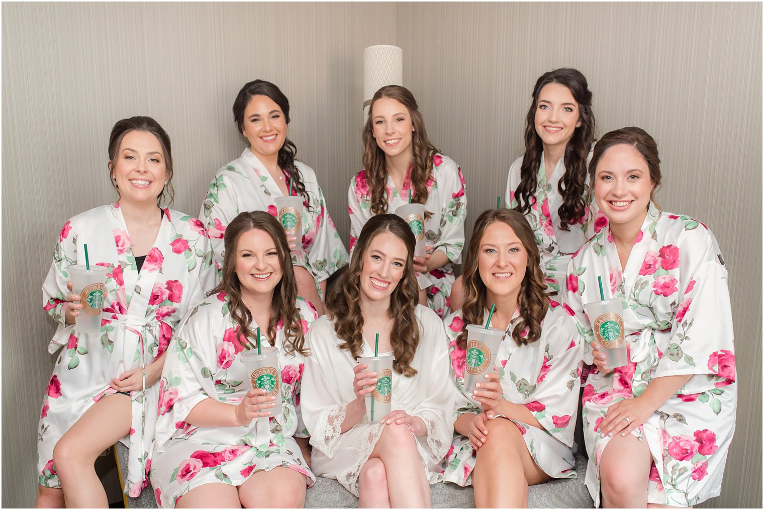 bride poses with bridesmaids in floral robes and starbucks cups