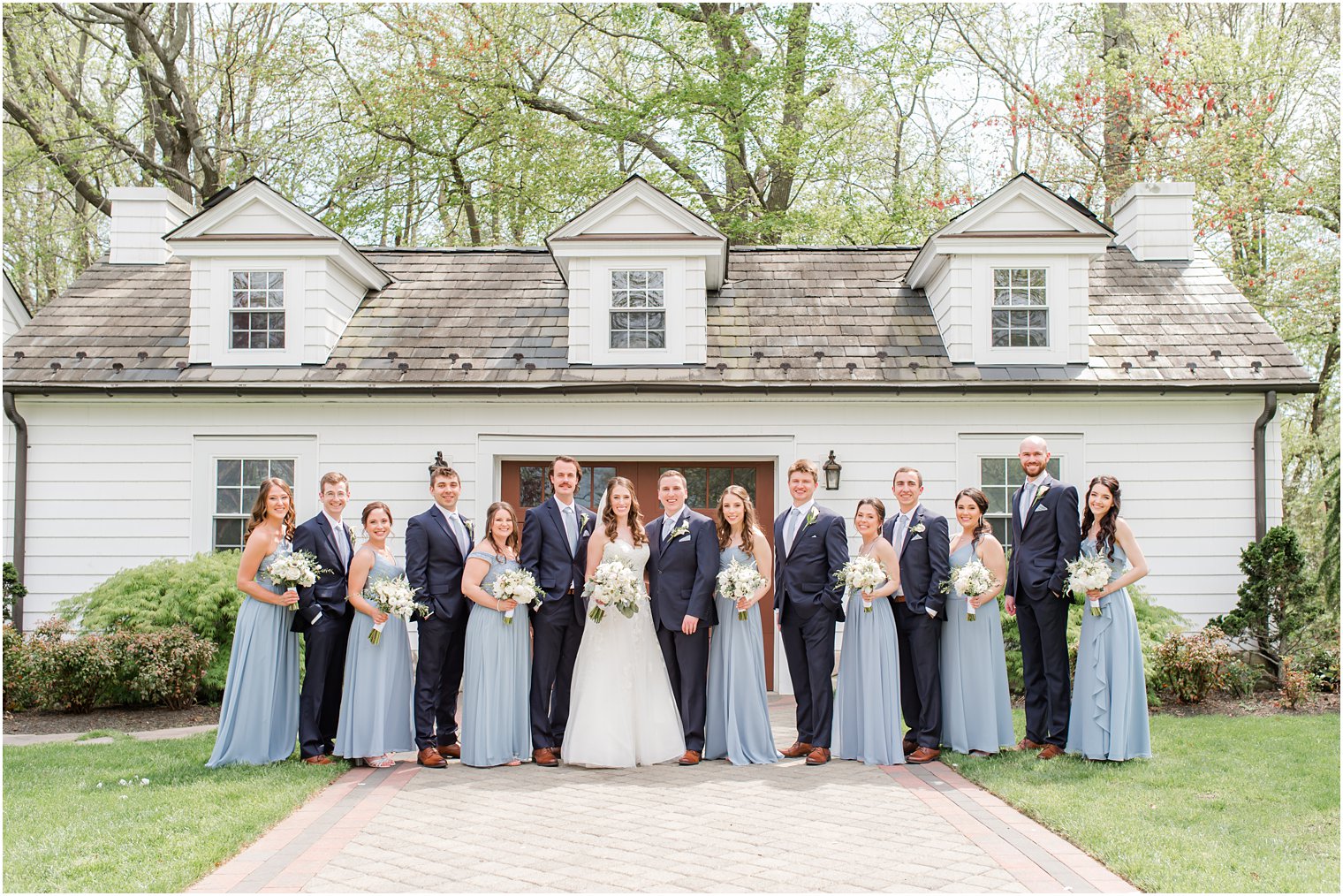 newlyweds pose with bridal party in blue suits and light blue dresses before spring English Manor wedding