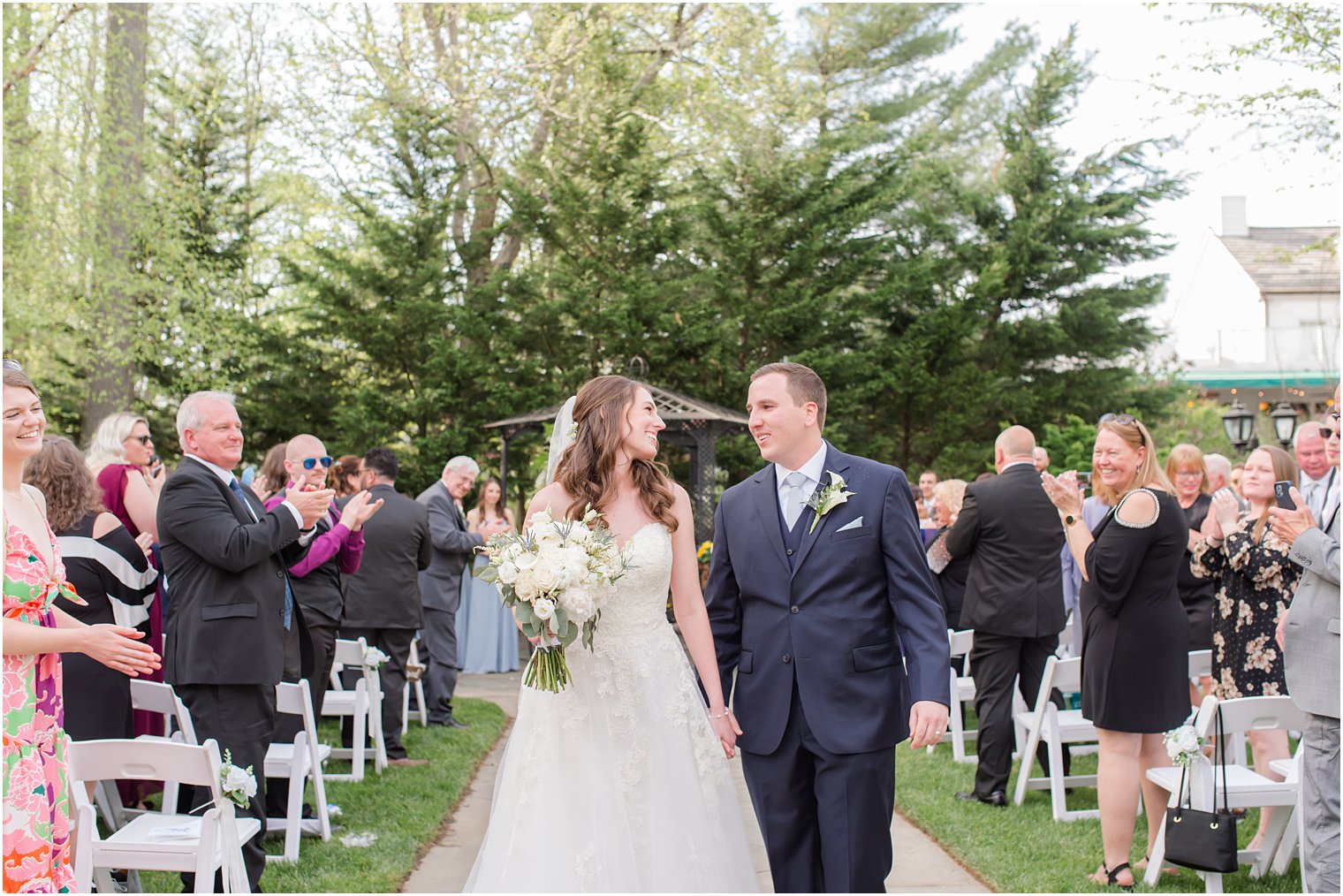 bride and groom smile at each other walking up aisle at spring English Manor wedding