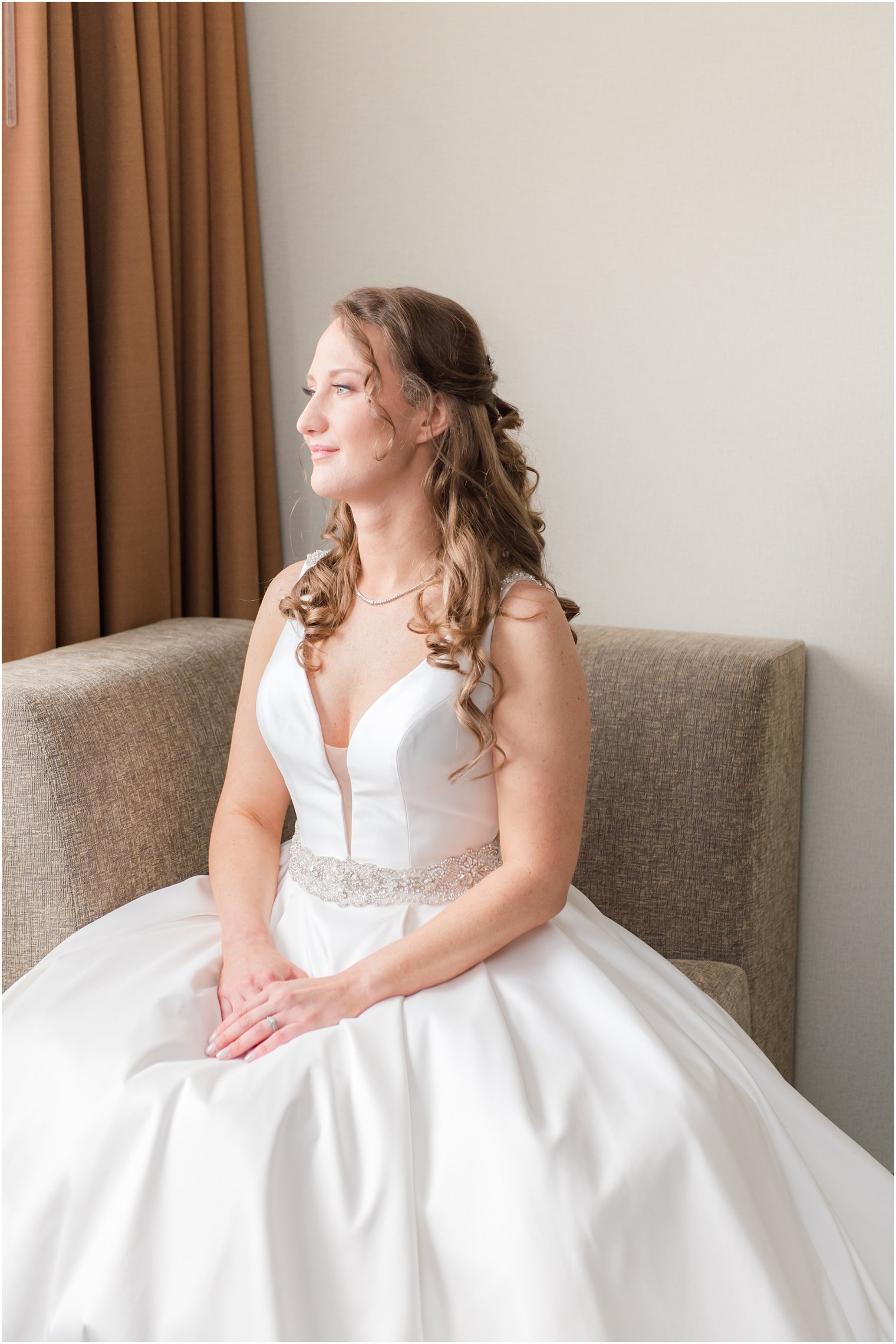 bride sits in chair at hotel room before Forsgate Country Club wedding 