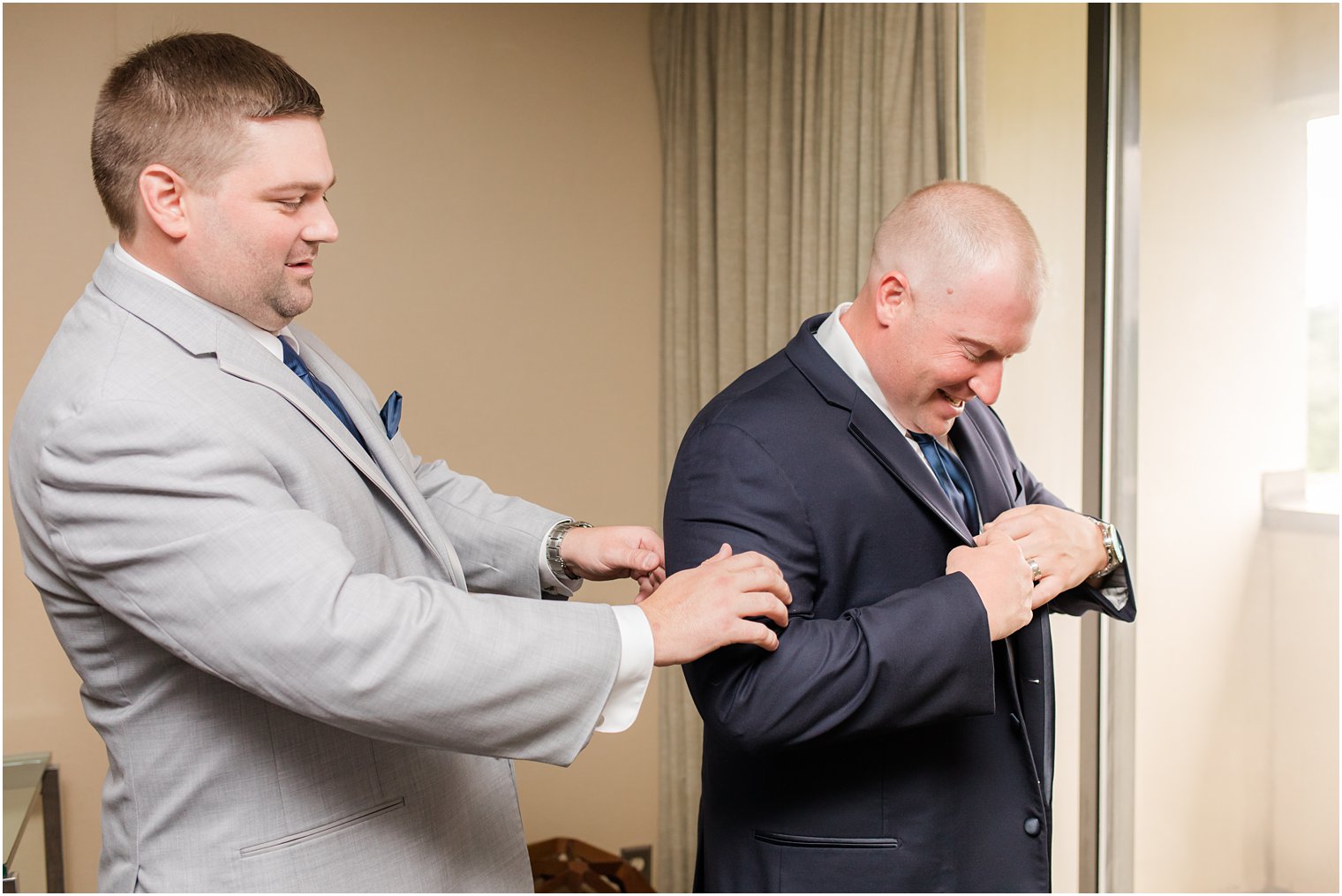 groomsman helps groom adjust suit jacket before Forsgate Country Club wedding 