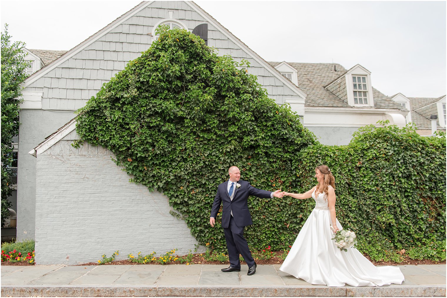 newlyweds walk by ivy covered wall in Forsgate Country Club