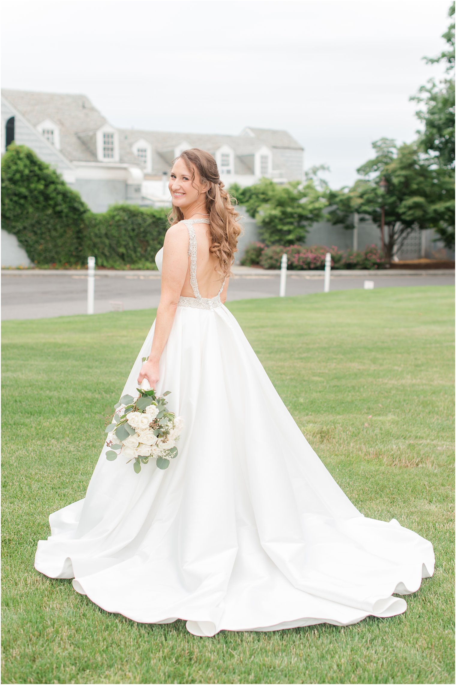 bride holds all-white bouquet by her side looking over her shoulder in wedding gown 