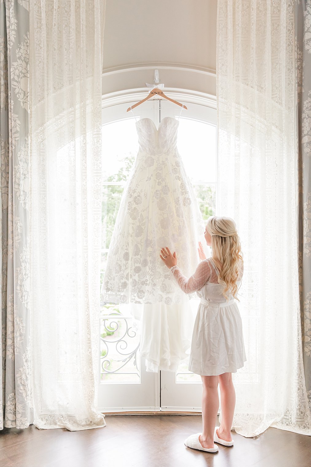 bride looks at wedding dress hanging in window at Park Chateau Estate