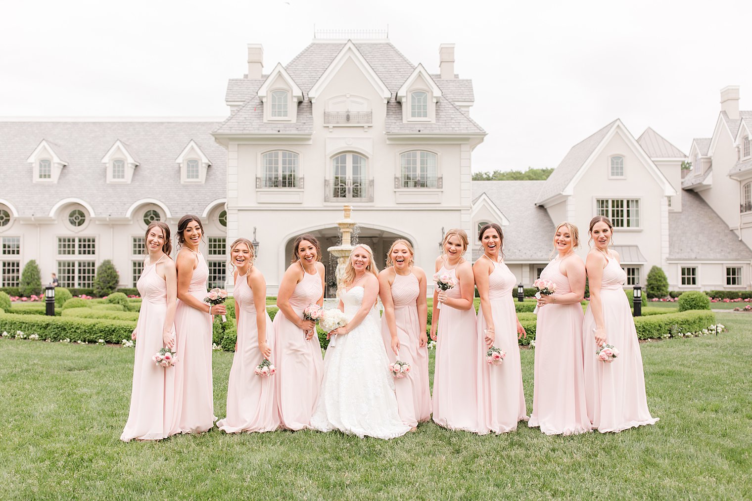 bride and bridesmaids laugh together in pale pink gowns