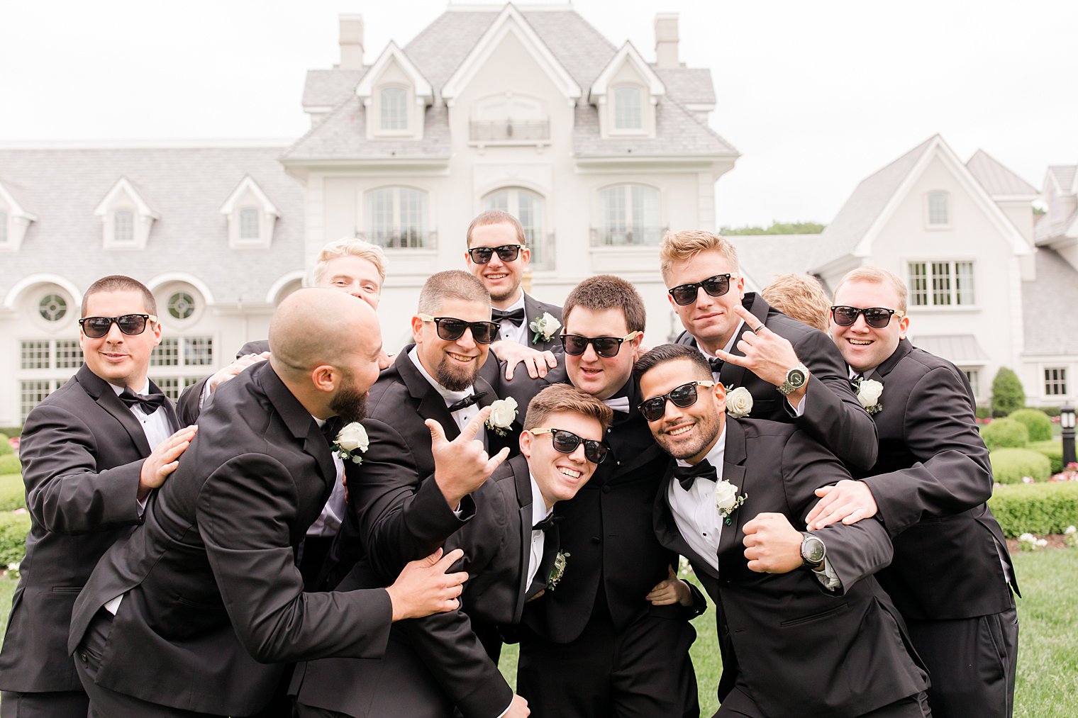 groom and groomsmen in sunglasses hug on lawn