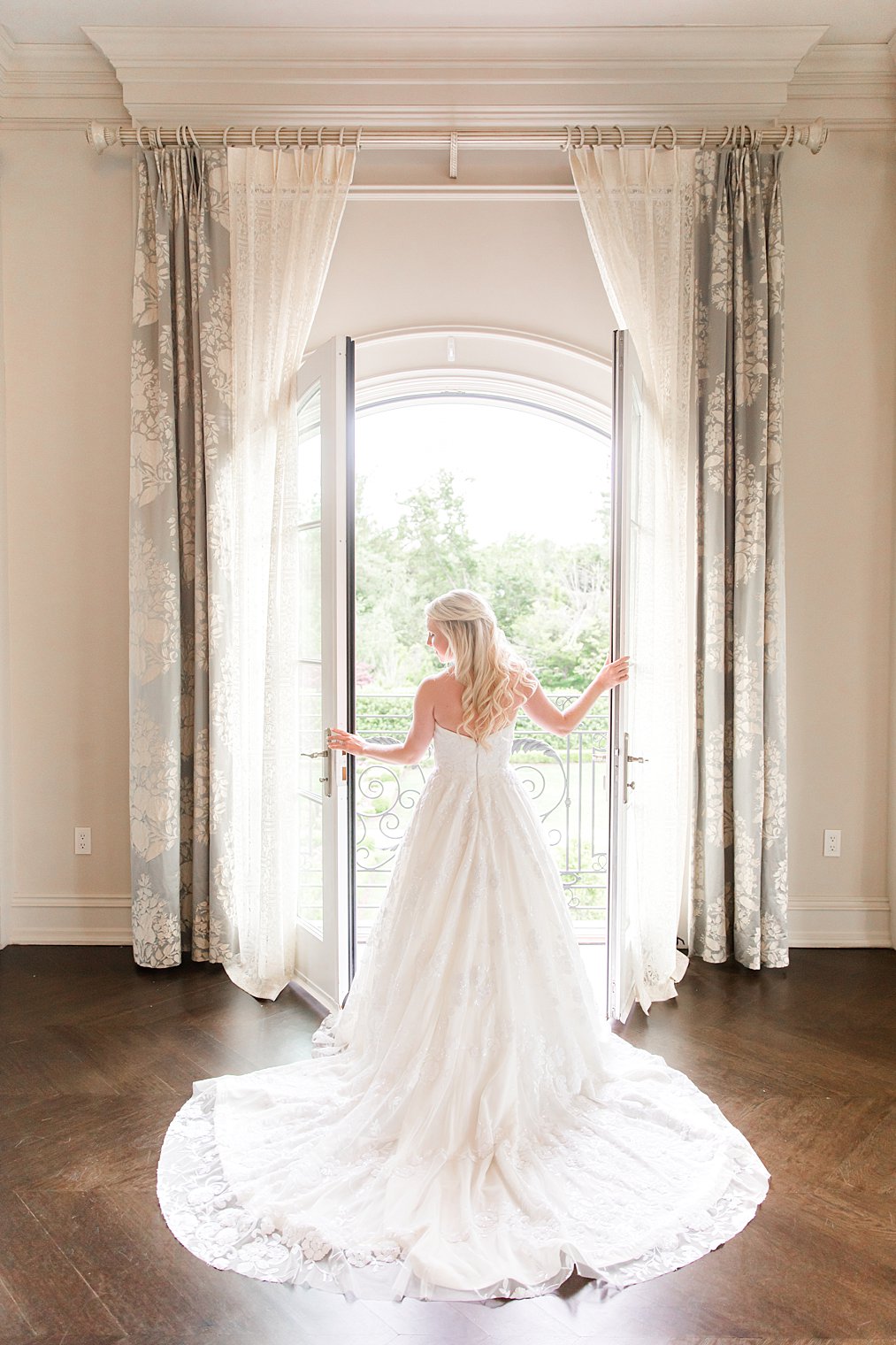 bride poses in bridal suite with train behind her looking out window