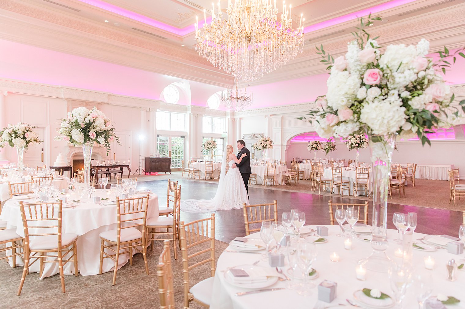 newlyweds dance together in ballroom at Park Chateau Estate with pink and white floral centerpieces