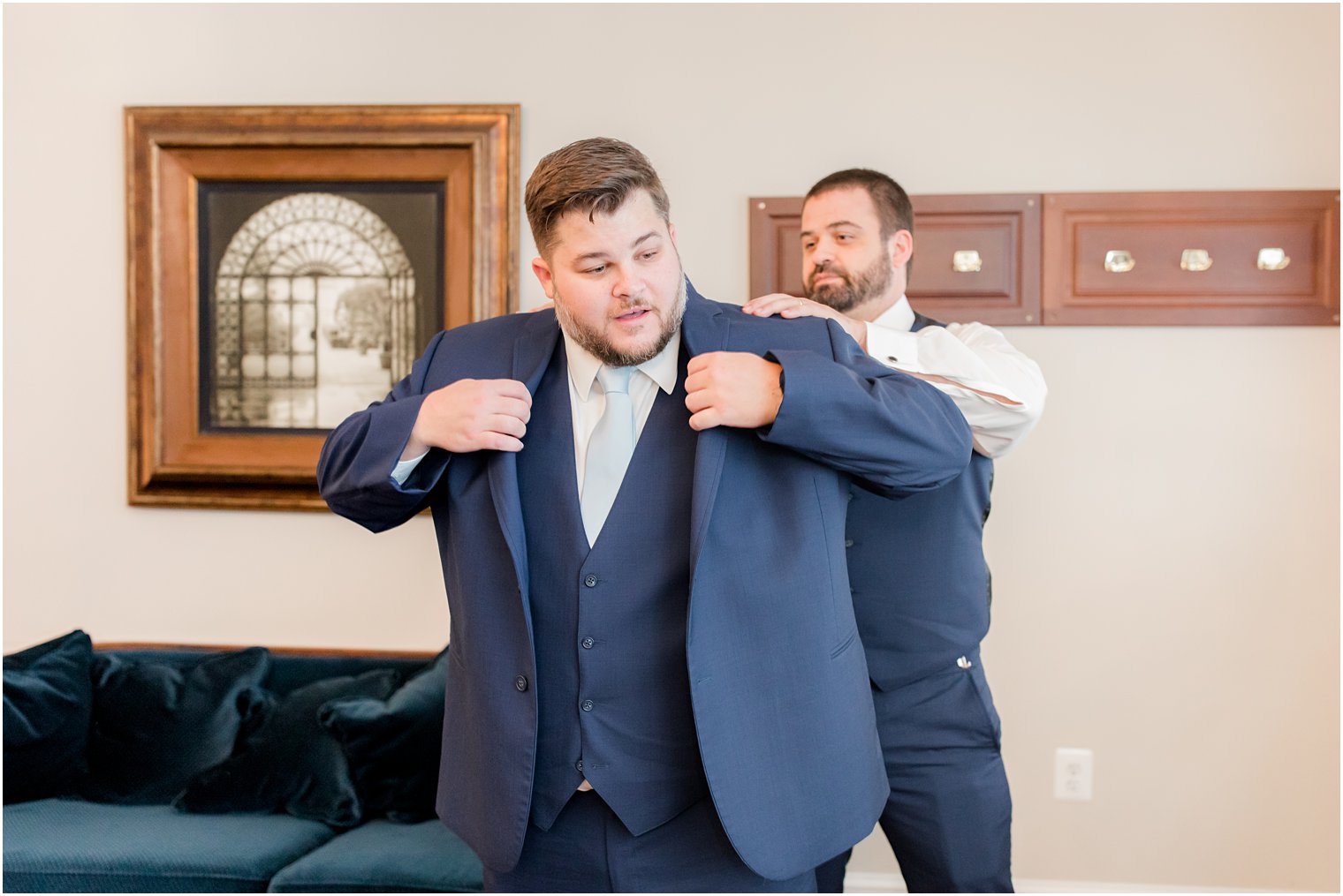 groomsman helps groom into navy suit jacket 