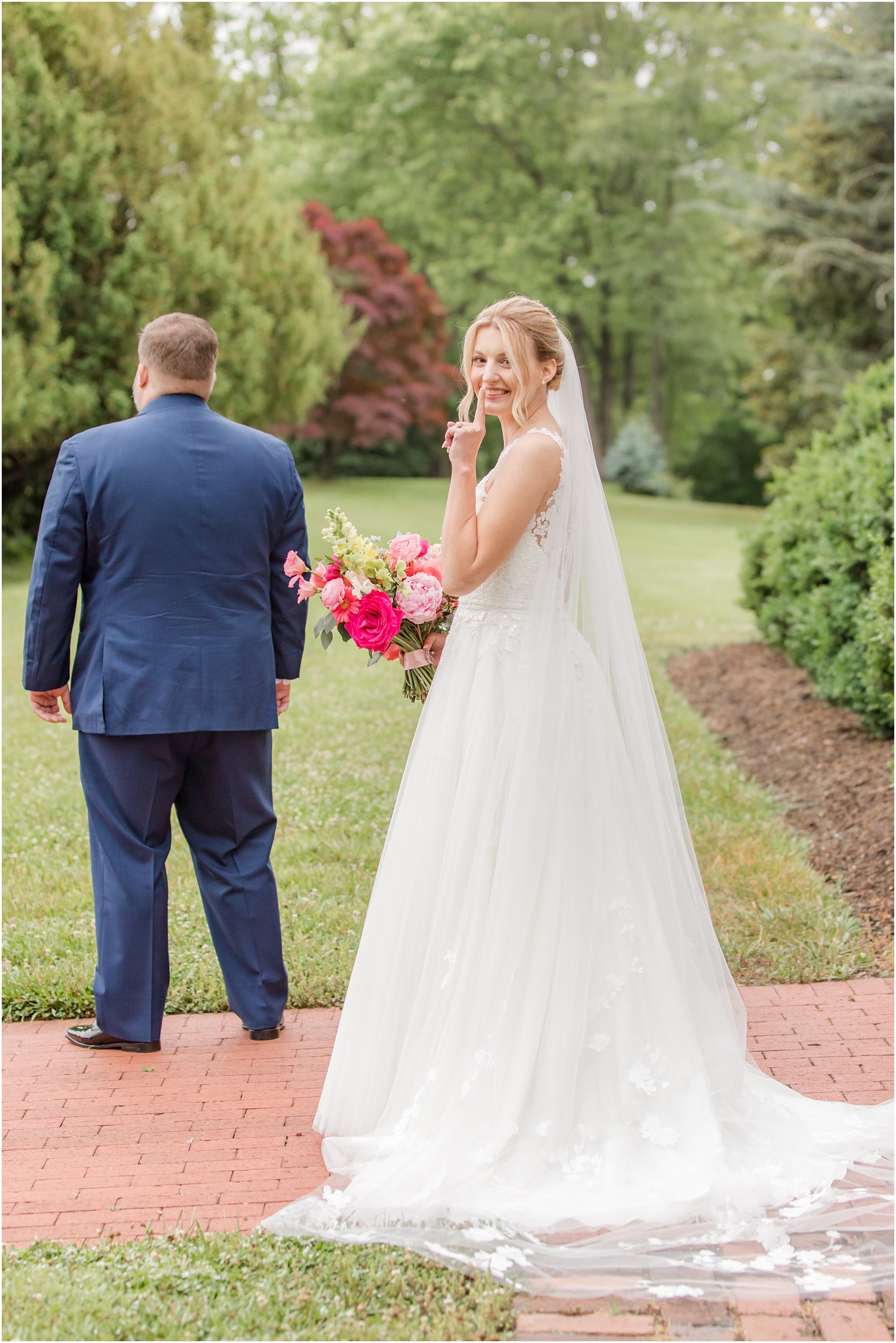 bride walks up behind groom shushing herself with finger on lips 