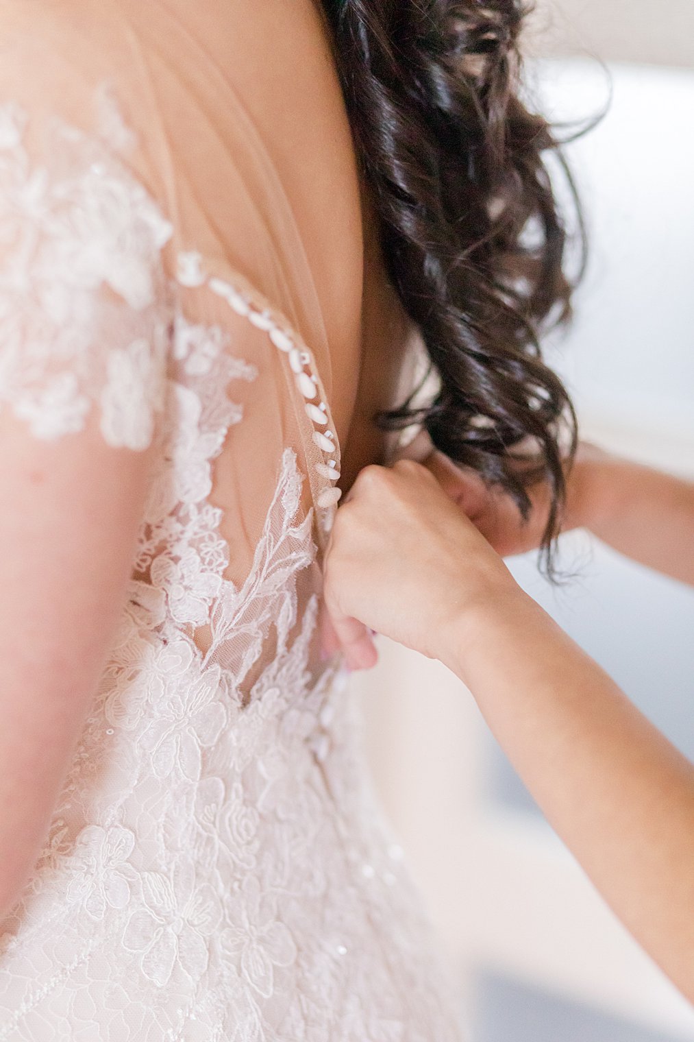 bridesmaid helps bride with buttons on wedding gown