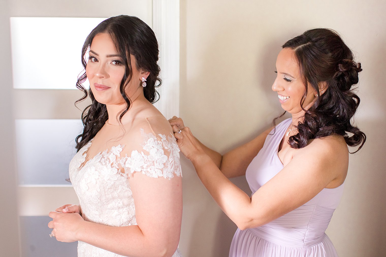 bridesmaid helps bride with wedding dress buttons