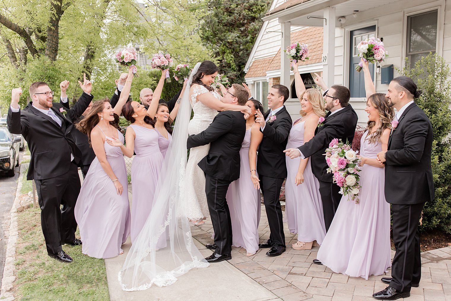 wedding party cheers while groom lifts bride up during Staten Island wedding