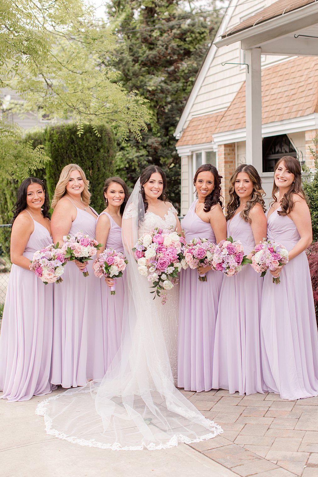 bride poses with bridesmaids in lilac gowns outside home 