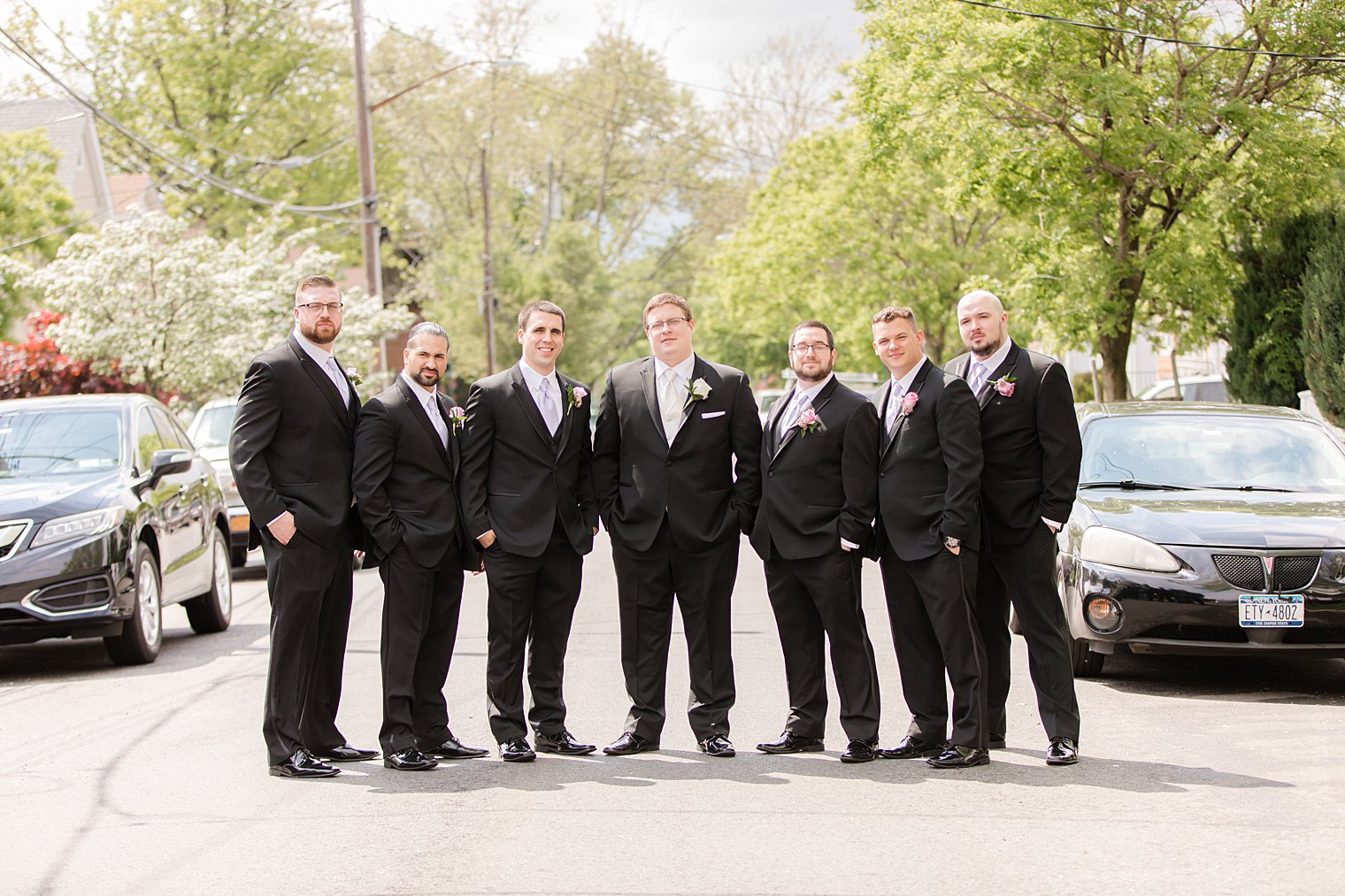 groom poses with six groomsmen in classic black suits in neighborhood 