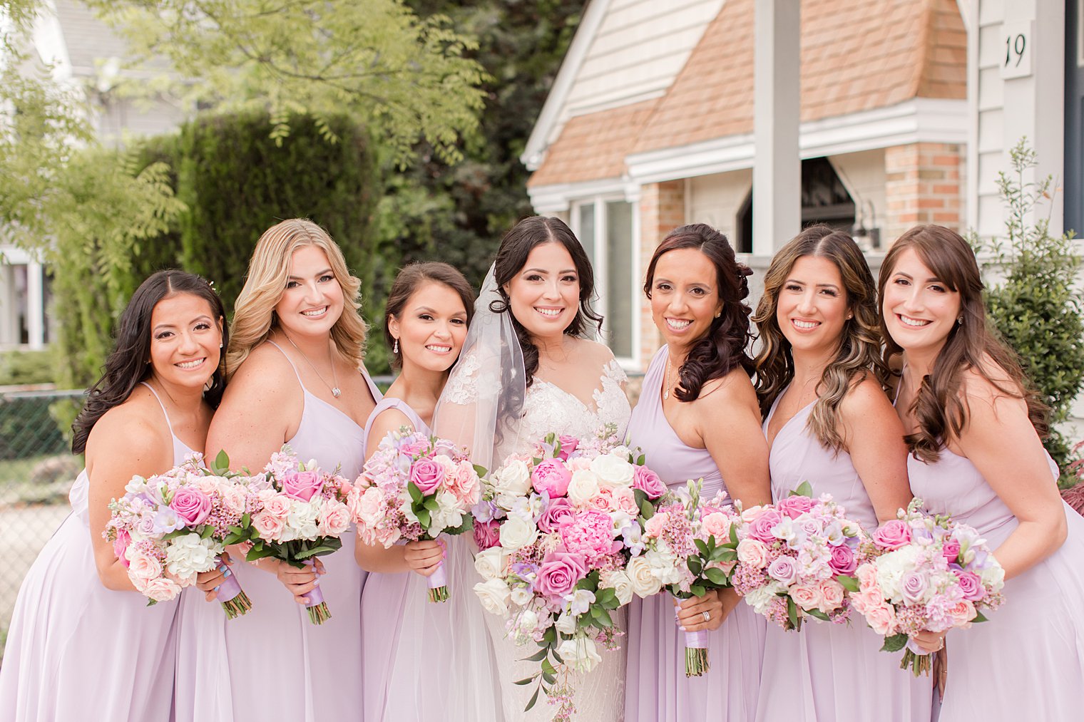 bride poses with bridesmaids in pink gowns with pink and purple bouquets 