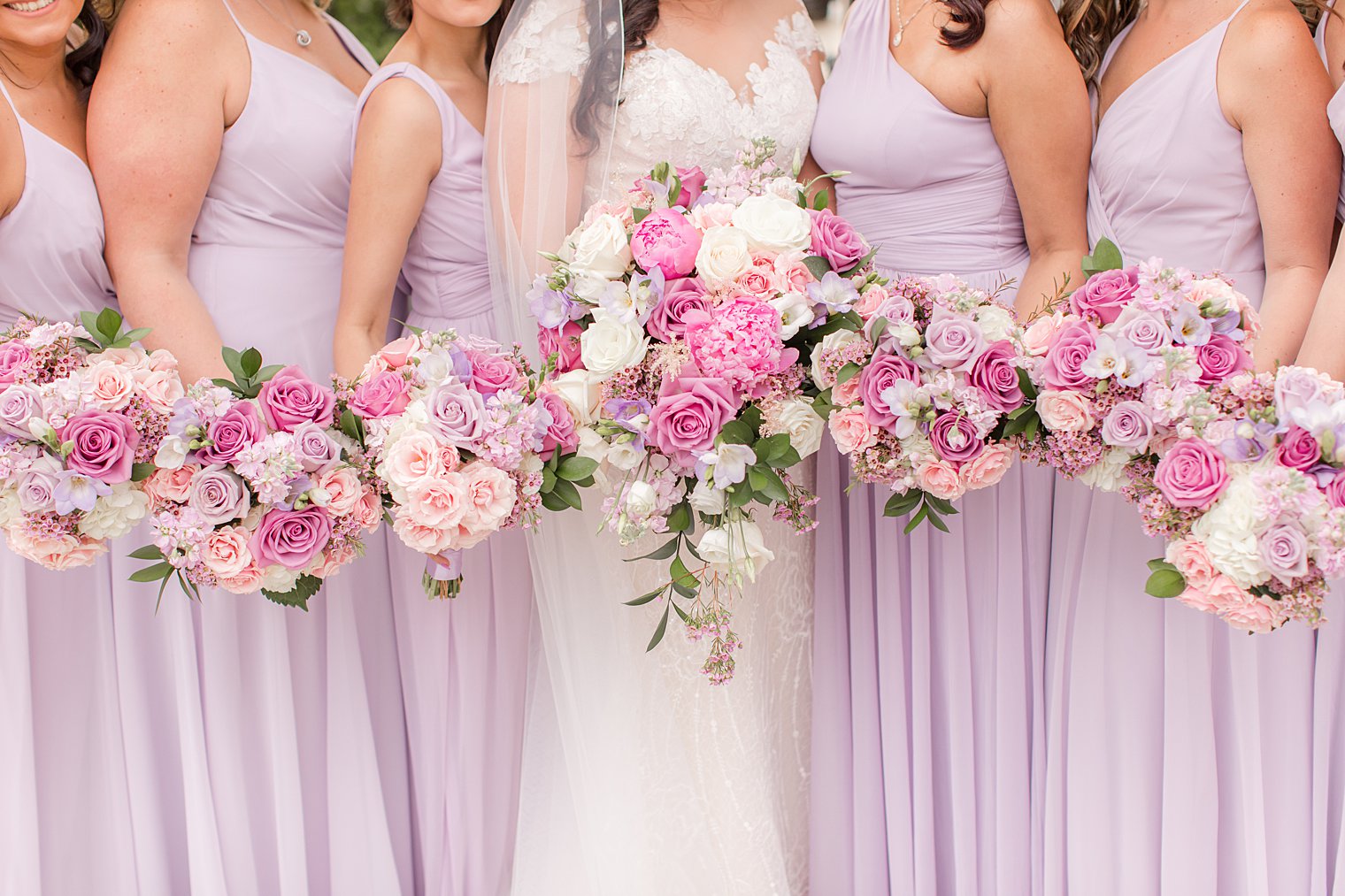 bride poses with bridesmaids in lilac gowns with pink and purple wedding bouquets 