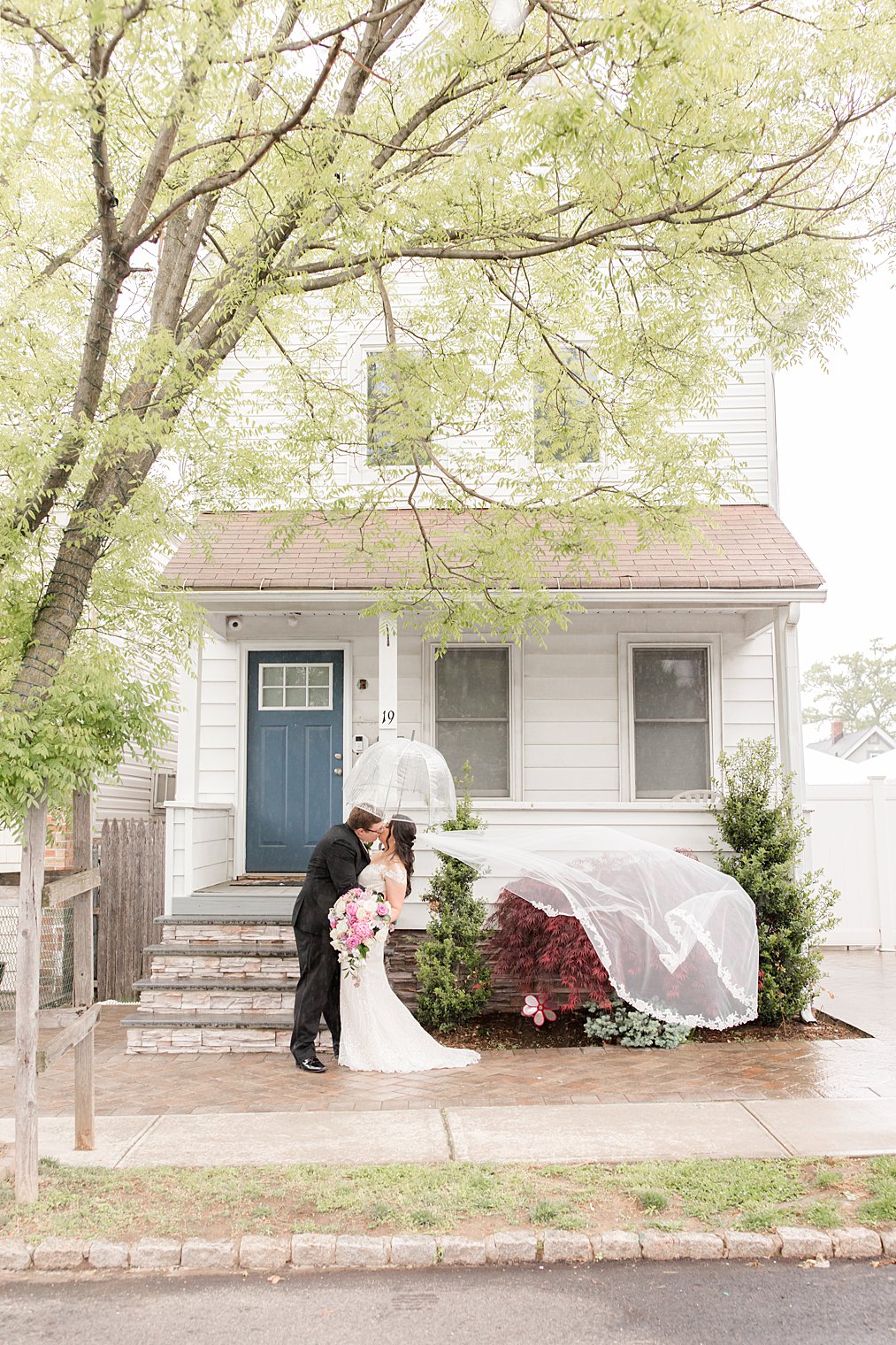 bride and groom pose under umbrella during rainy wedding day at home in Staten Island NY 