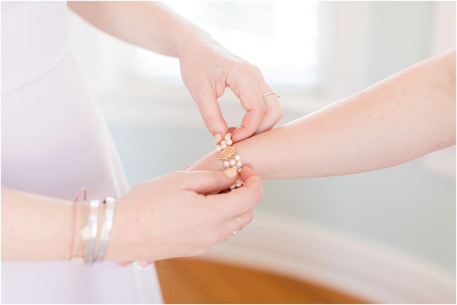bridesmaid helps bride with pearl bracelet 