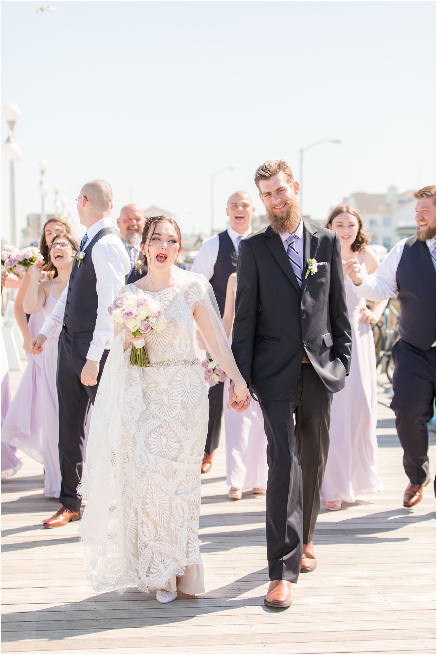 newlyweds walk down boardwalk with bridal party on beach