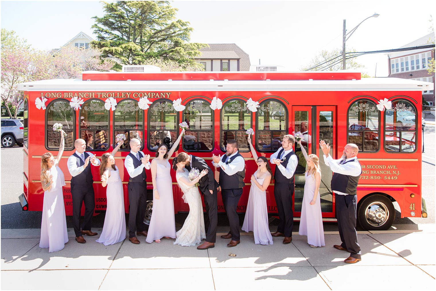 bride and groom kiss outside red trolley with bridal party cheering