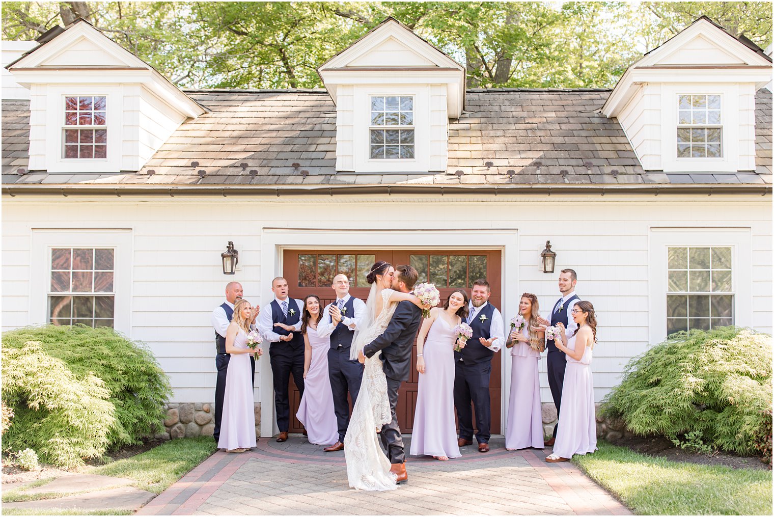 bride and groom kiss with bridal party cheering behind them outside The English Manor