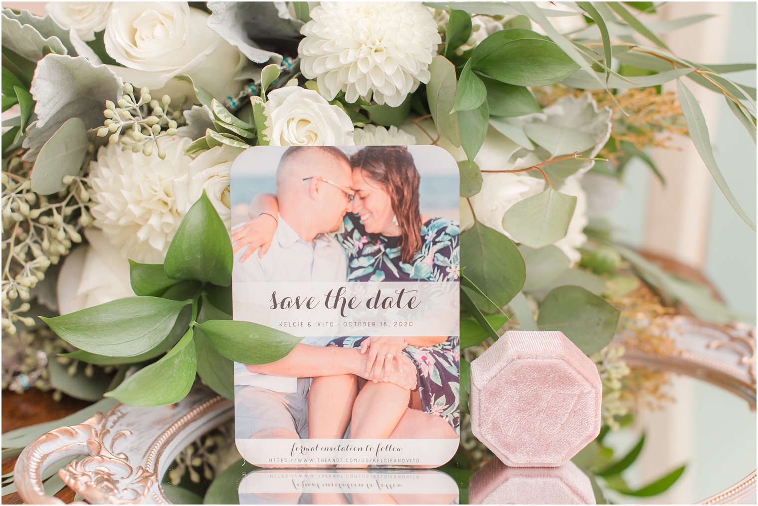 save the date card rests on bouquet with pink ring box