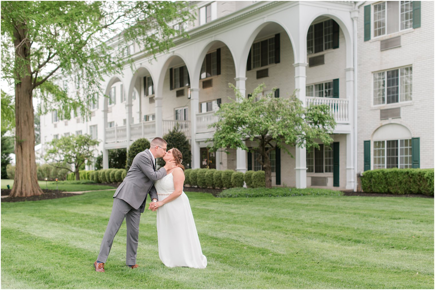 groom kisses bride during New Jersey wedding photos in front of white historic hotel