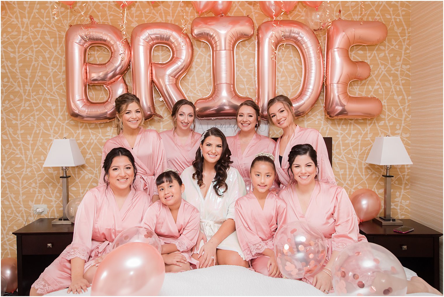 bride sits on bed with bridesmaids under BRIDE Balloons