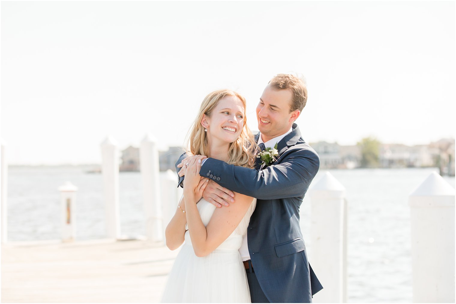 groom hugs bride from behind during NJ wedding portraits on pier 