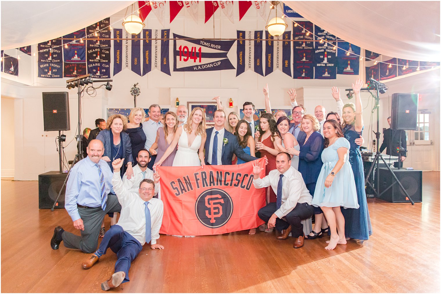 couple poses with guests and San Francisco flag at Bay Head Yacht Club wedding reception 