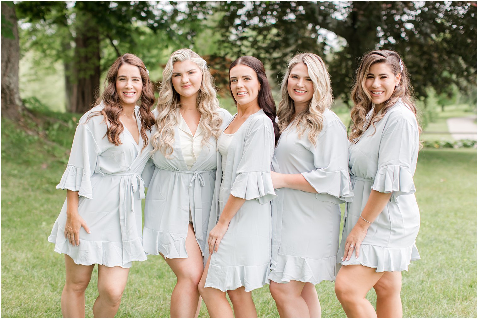 bridesmaids in light blue robes outside smiling at the camera