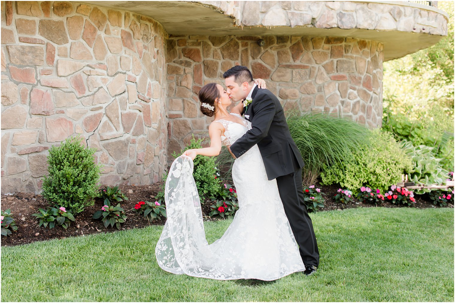 groom kisses bride leaning her back while she holds tail of dress up 